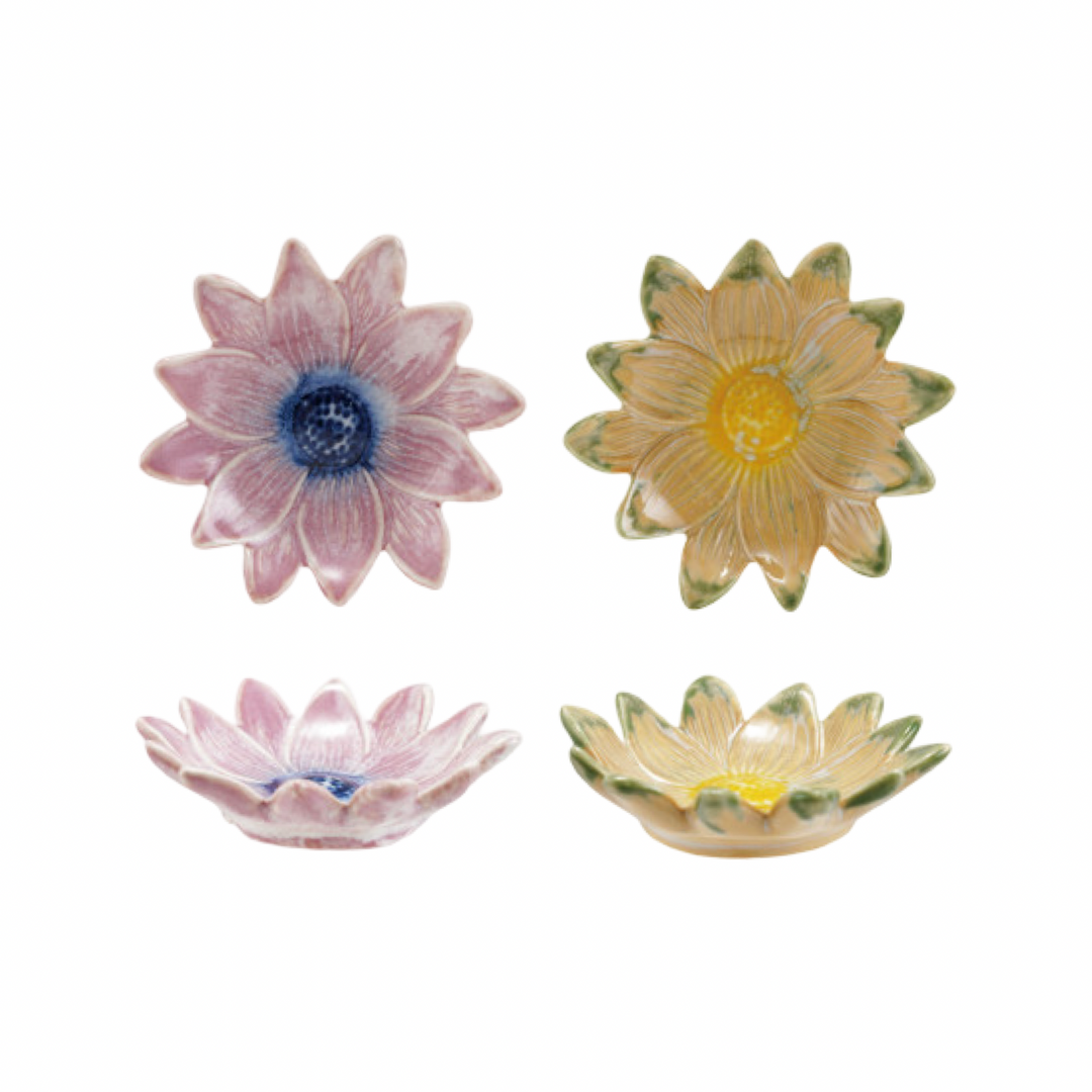 Two stoneware daisy-shaped dishes shown from top and side view, in pink with a blue center and golden yellow with green petal tips.