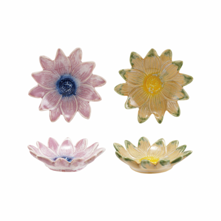 Two stoneware daisy-shaped dishes shown from top and side view, in pink with a blue center and golden yellow with green petal tips.