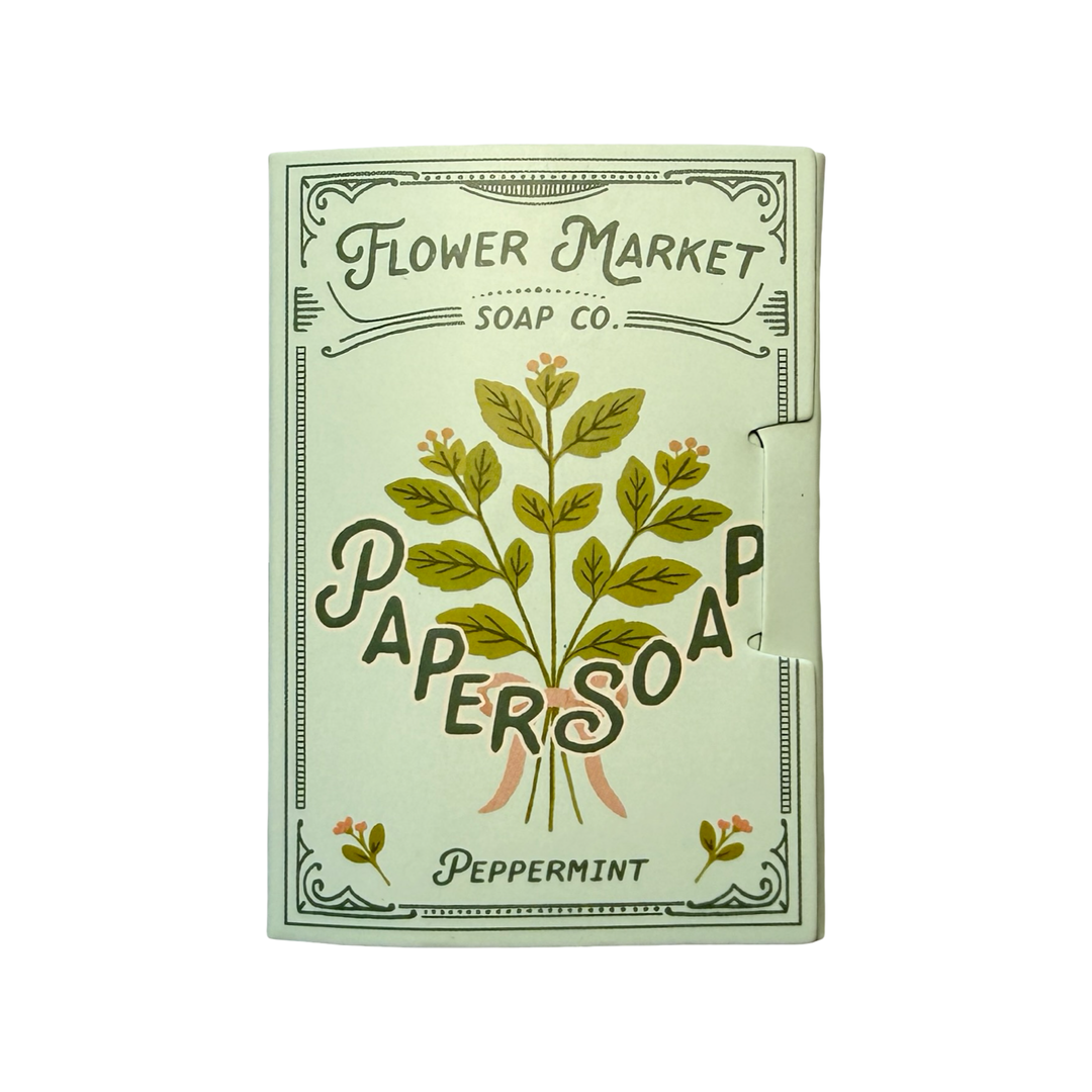A white booklet of Flower Market Soap Co. Peppermint Paper Soap with a botanical illustration of a mint sprig tied with a pink ribbon.
