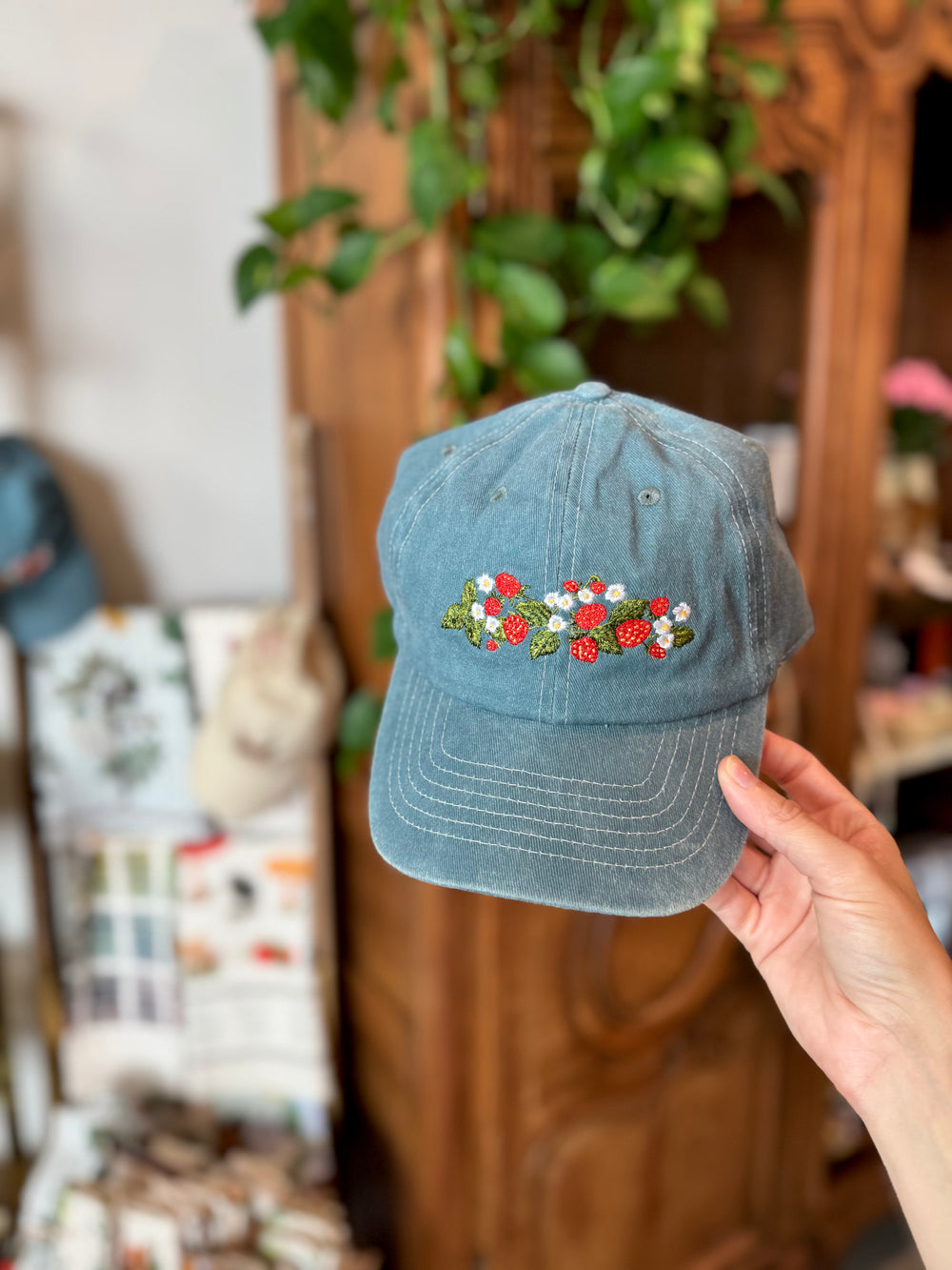 Blue denim cap with floral embroidery held in front of a store display.