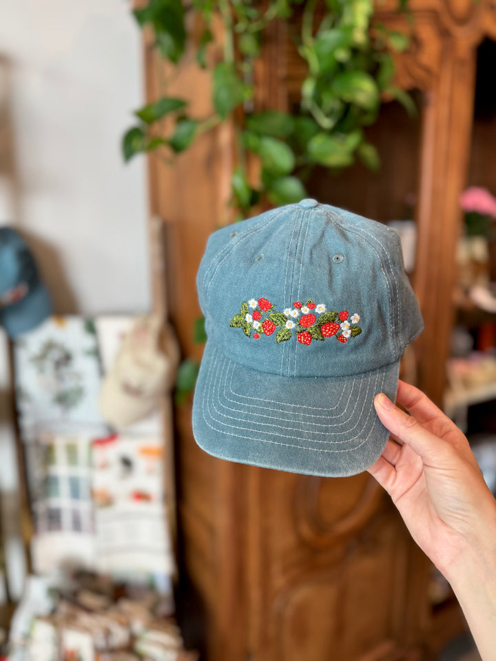 Blue denim cap with floral embroidery held in front of a store display.