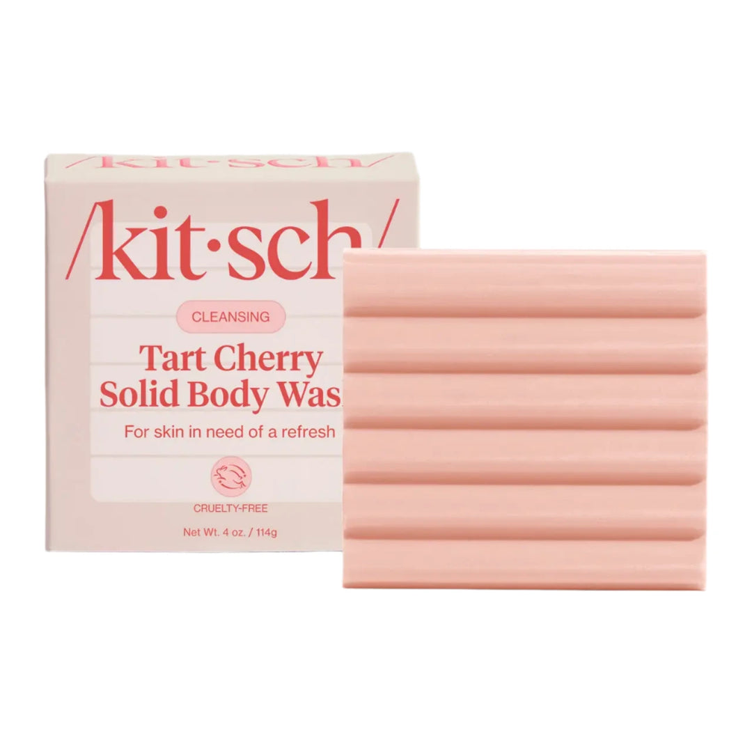 A light pink solid body wash bar with horizontal ridges, shown next to its packaging labeled “Kitsch Tart Cherry Solid Body Wash” with a note for refreshing skin.