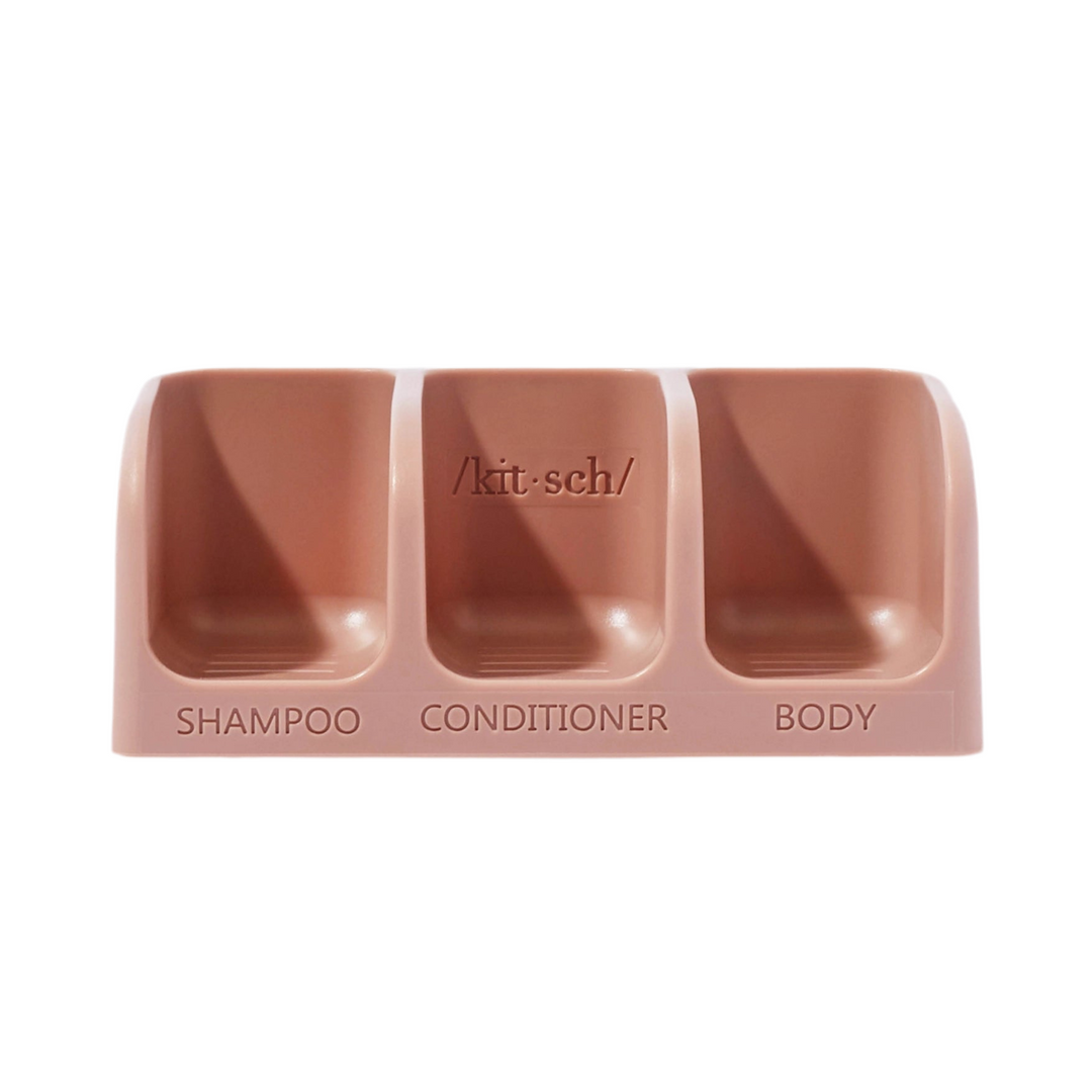 front view of a light pink soap dish that has three compartments with the words shampoo, conditioner and body at each compartment.