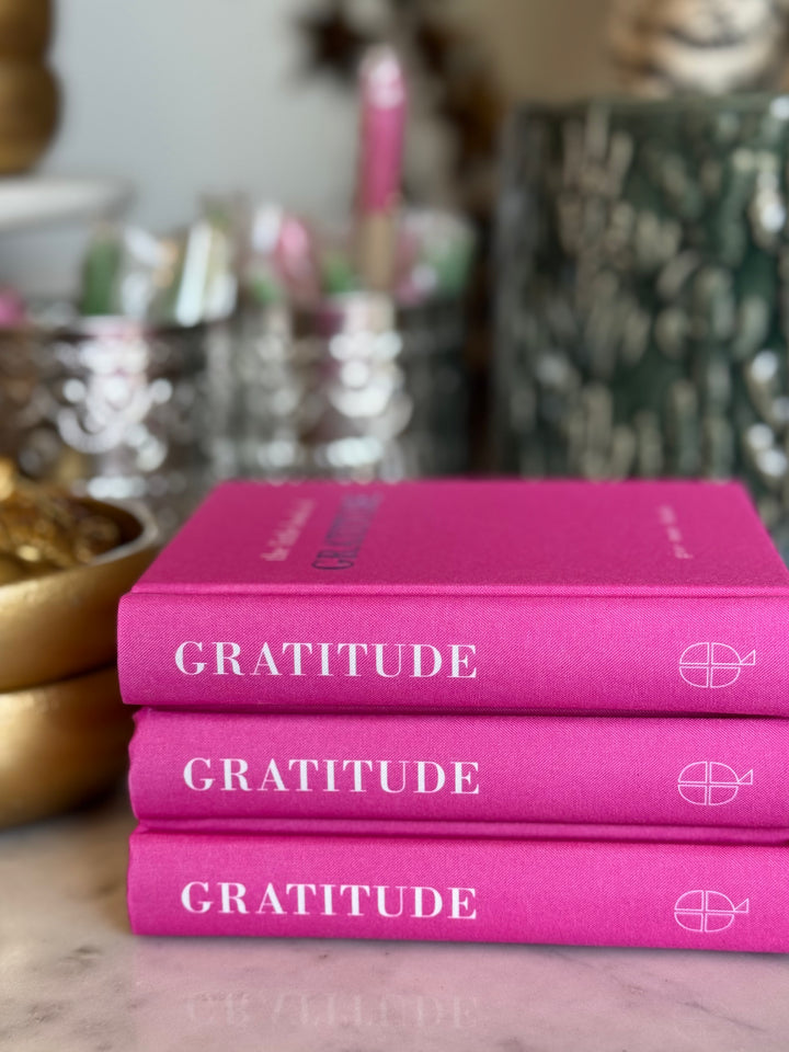 Stack of pink books titled 'Gratitude' on a surface with a blurred background