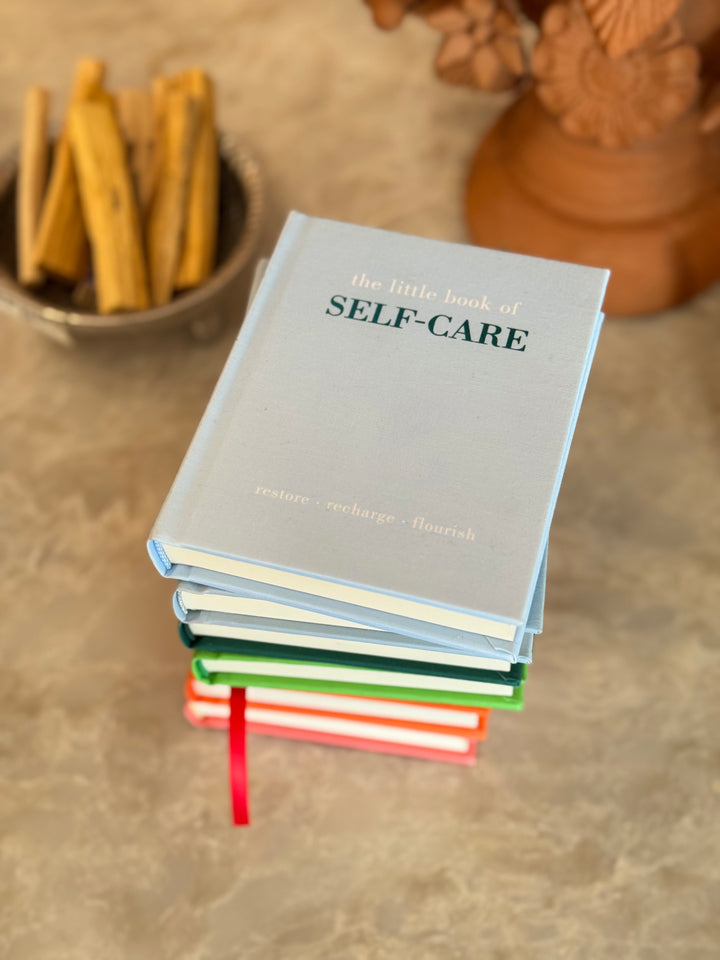 Stack of books titled 'the little book of SELF-CARE' on a textured surface.