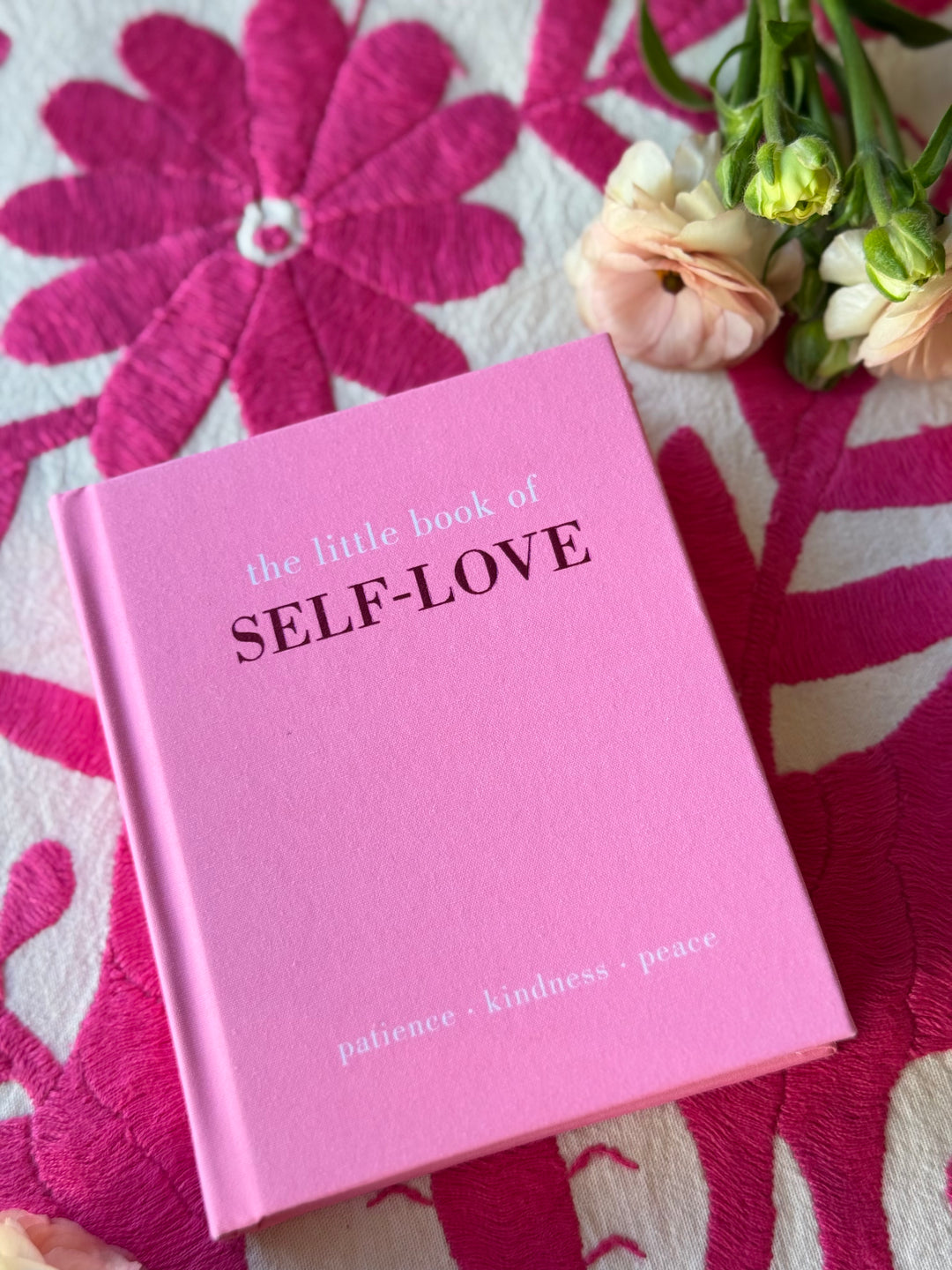 Pink book titled 'the little book of SELF-LOVE' on a floral fabric background