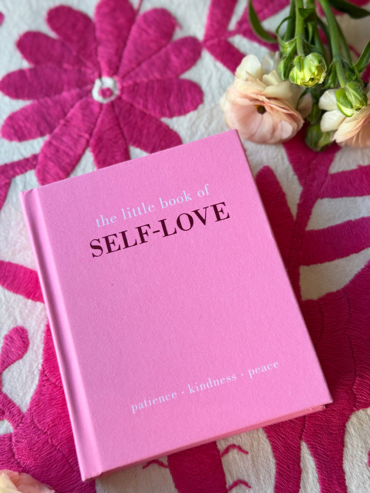 Pink book titled 'the little book of SELF-LOVE' on a floral fabric background