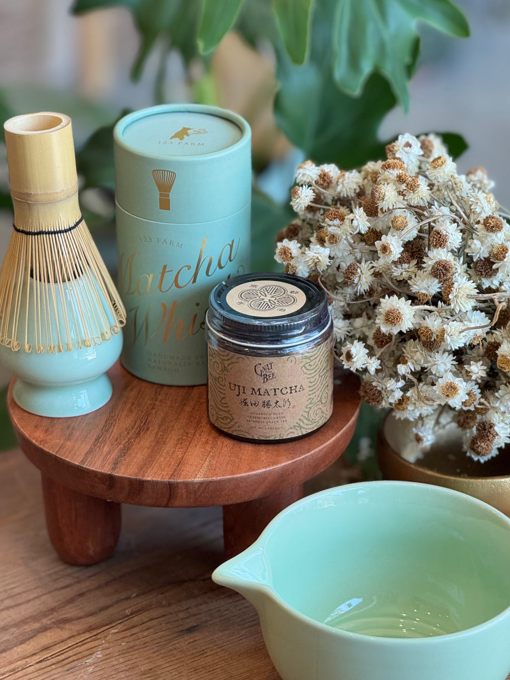 Matcha tea set with a wooden stand, green bowl, and matcha whisk on a wooden surface.