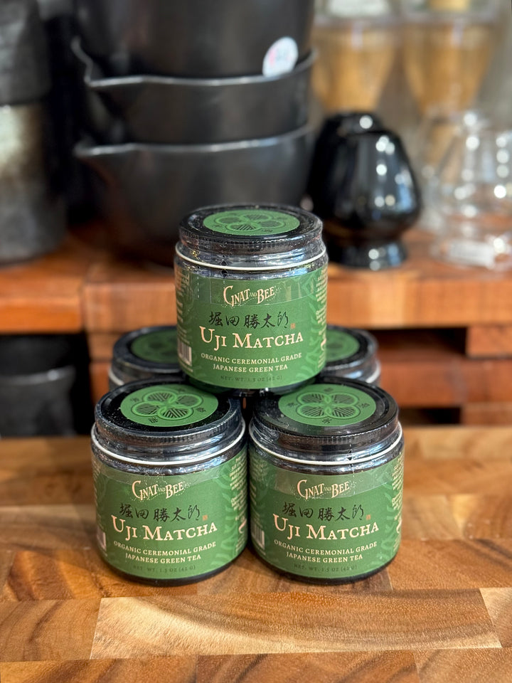 Jars of Uji Matcha green tea stacked on a wooden surface with kitchen items in the background.