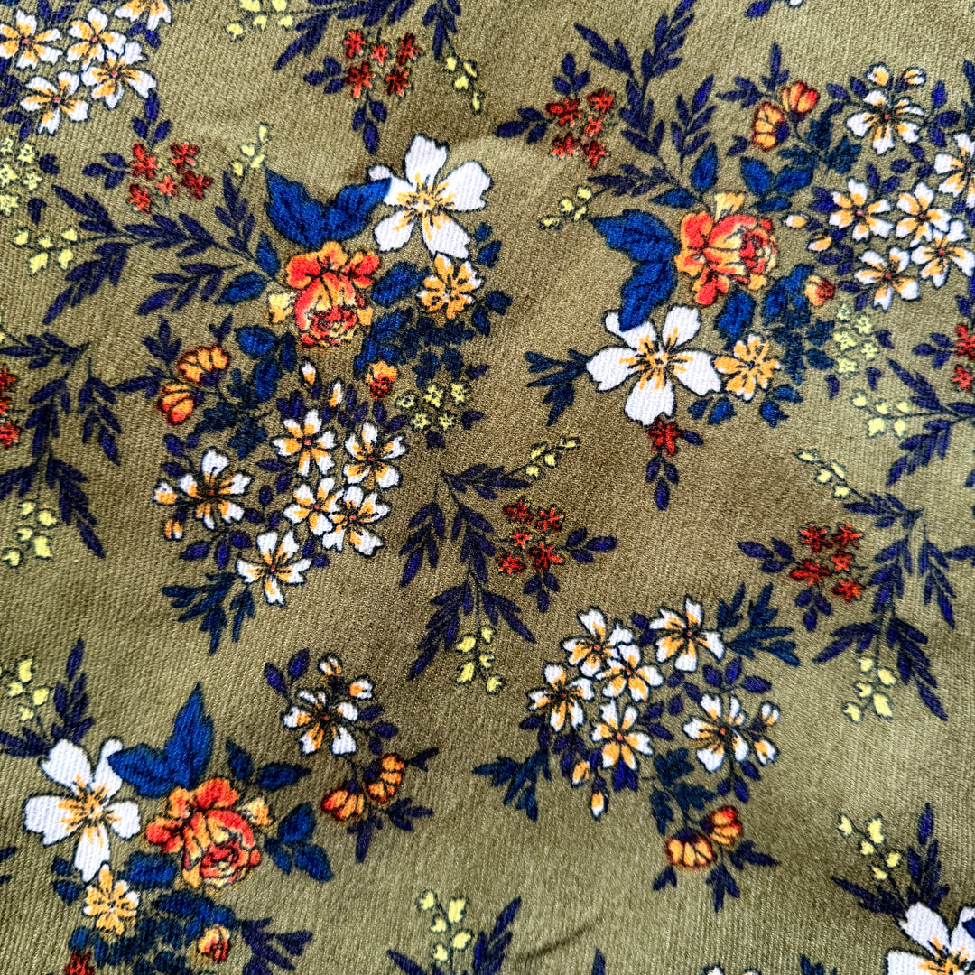 Close view of forest green corduroy fabric features white, blue, orange and yellow floral pattern.