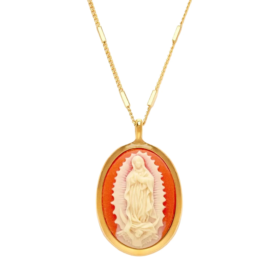 A close-up of an oval cameo pendant featuring a detailed relief carving of the Virgin of Guadalupe in cream tones against a rich coral background, framed in a polished gold oval bezel, hung on a mixed bar and curb link gold chain.