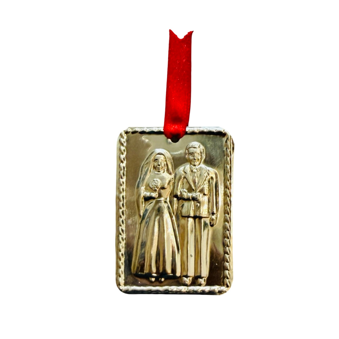 This milagro features a bride and groom in raised relief, framed by a twisted rope border and finished with a red ribbon.