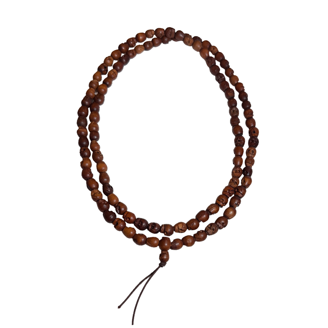 Long mala necklace made of hand-carved wooden skull beads strung on a dark cord with tassel ends.