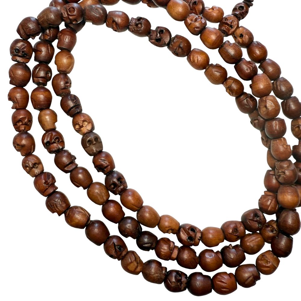 close up view of a Long mala necklace made of hand-carved wooden skull beads strung on a dark cord with tassel ends.