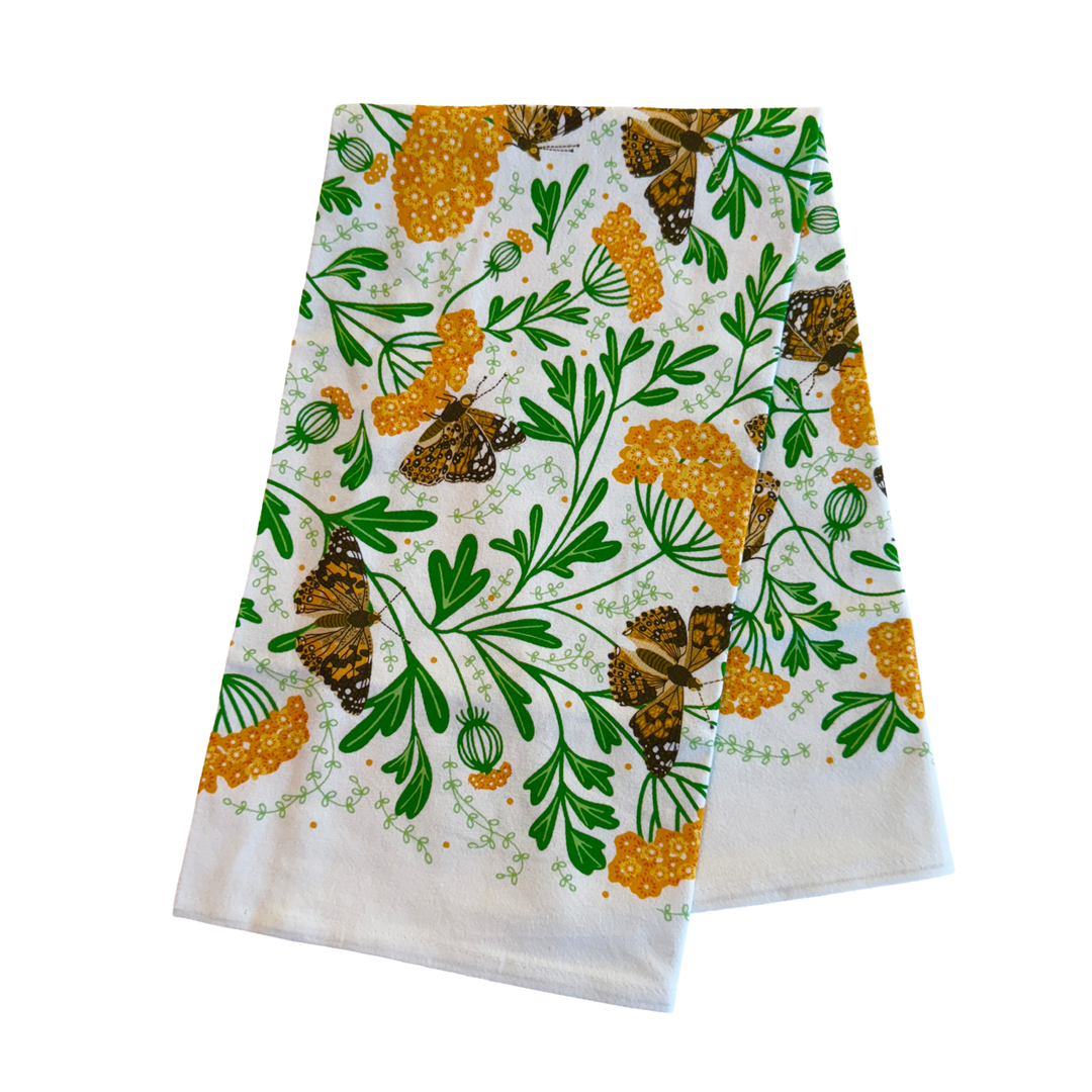 White cotton tea towel printed with a botanical pattern of golden yarrow flowers and painted lady butterflies, accented with green leaves folded in half.