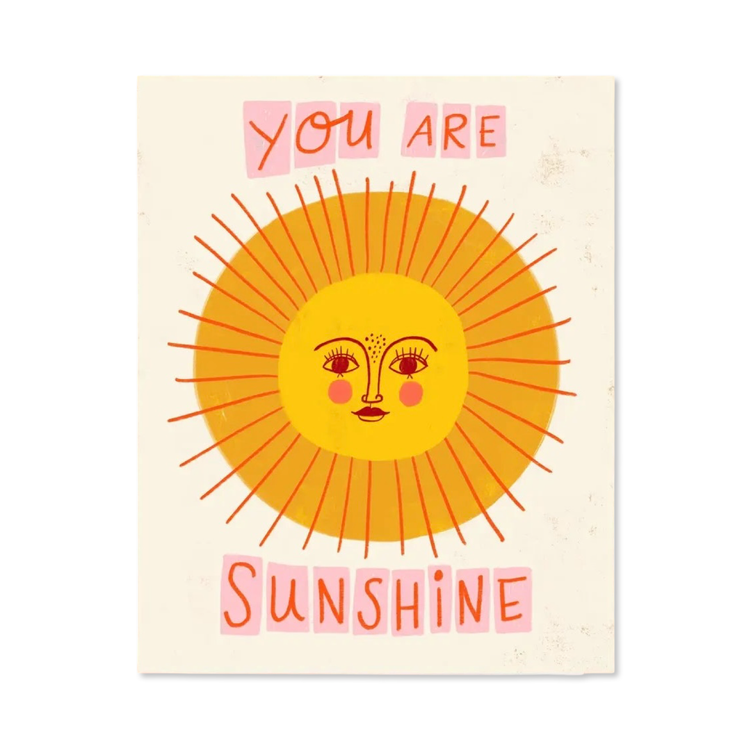 Greeting card with a bright illustrated sun face surrounded by orange rays. Above and below the sun, text reads “You Are Sunshine” in playful pink and orange lettering.