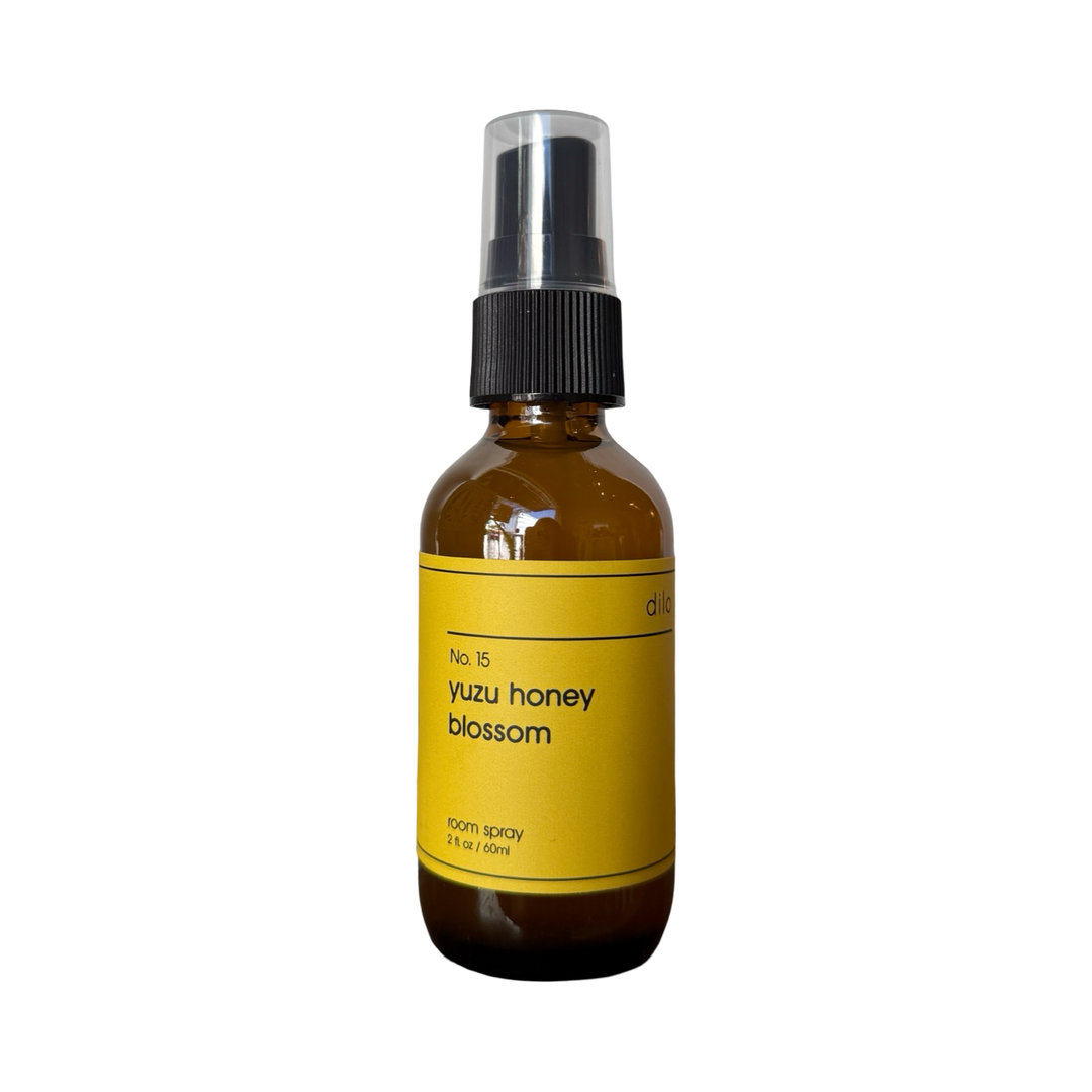 a 2 oz dark brown bottle of yuku honey blossom room spray featuring a dark yellow label with a black pump.