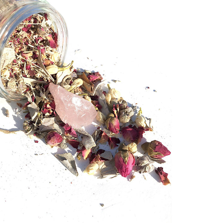 image of an open glass jar on its side with dried flowers and a quartz crystal spilling out of it.