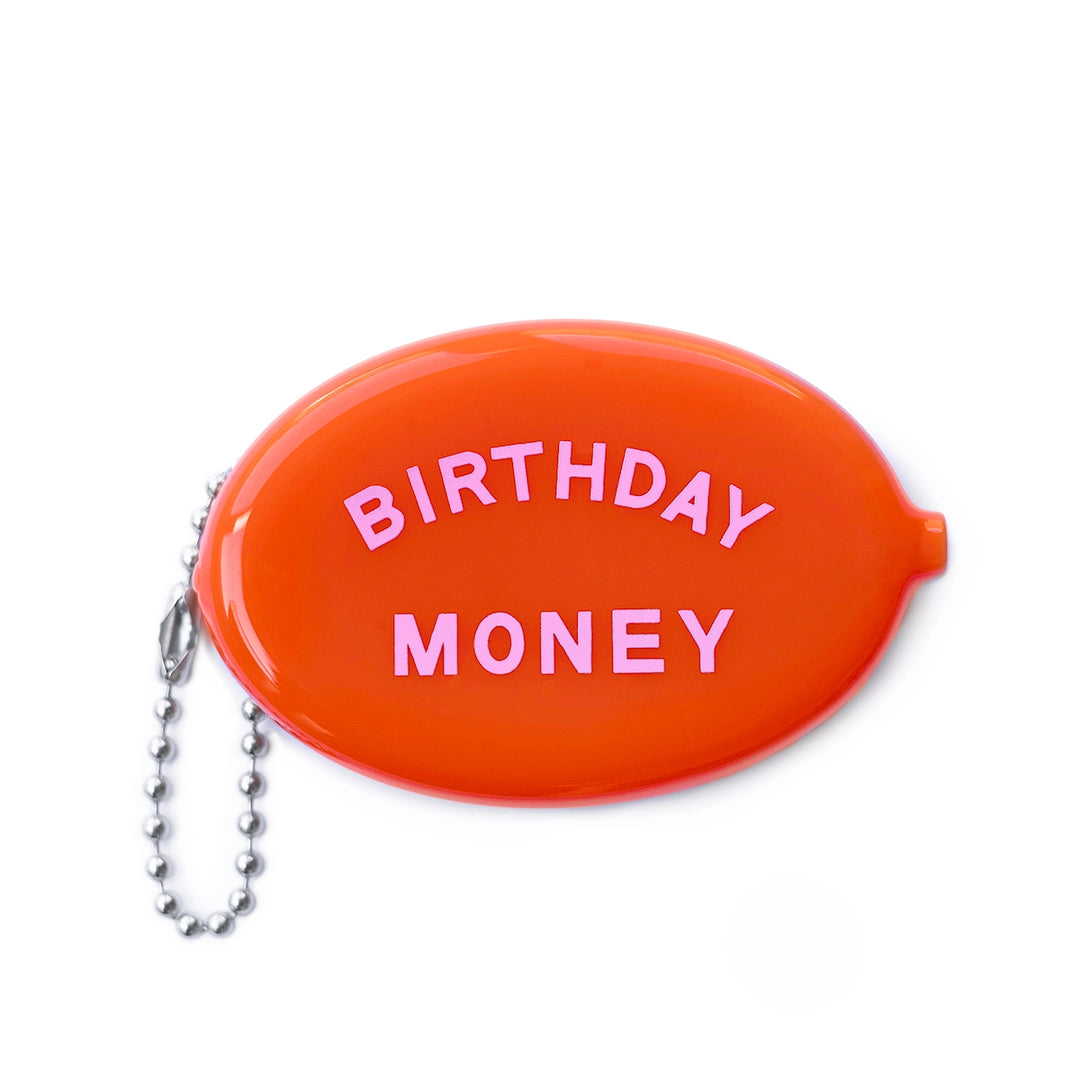 A bright orange oval coin pouch with the words "BIRTHDAY MONEY" written in bold pink letters, attached to a silver ball chain.