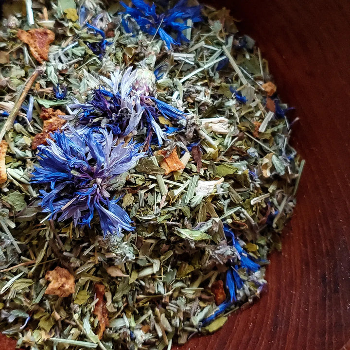 close up view of dried purple flower and loose leaf tea in a wooden bowl.