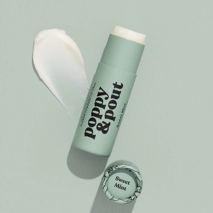 Tube of lip balm labeled “poppy & pout” with cap beside it and a swatch of balm nearby.
