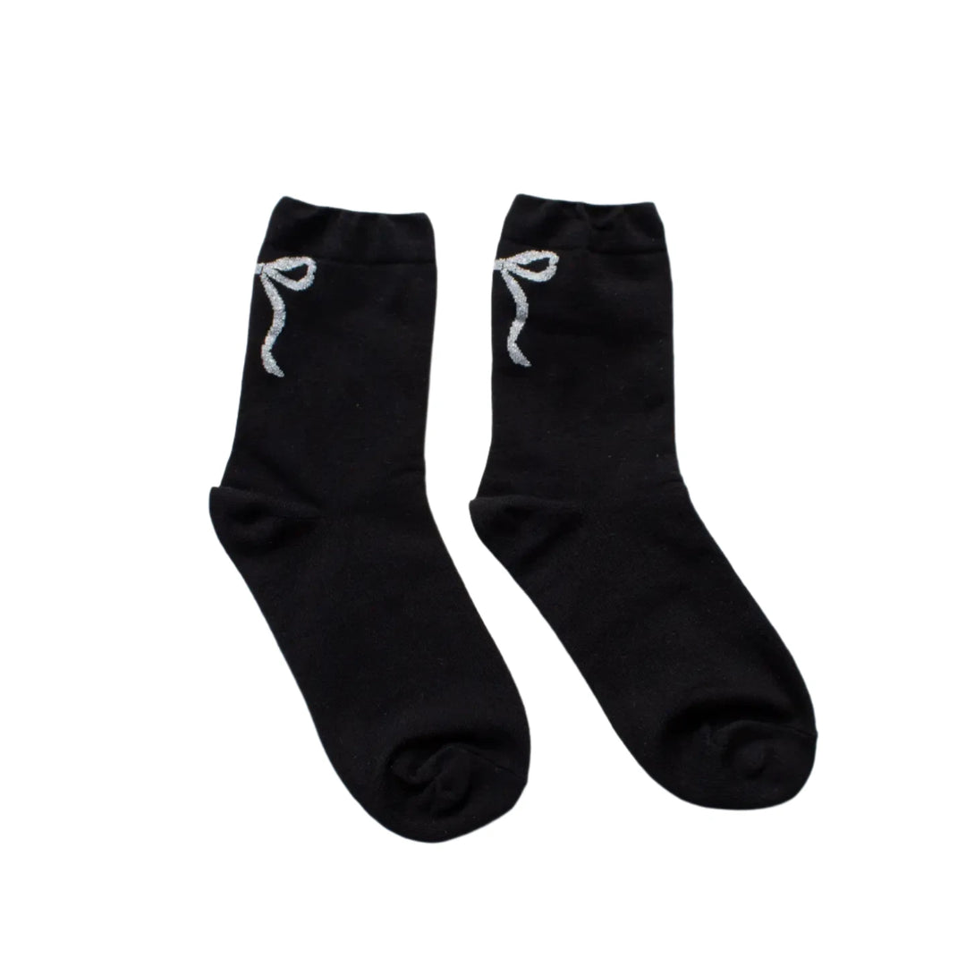 A pair of black socks with a glittery ribbon detail near the top, laid flat on a white textured background, showcasing their elegant and minimalist design.