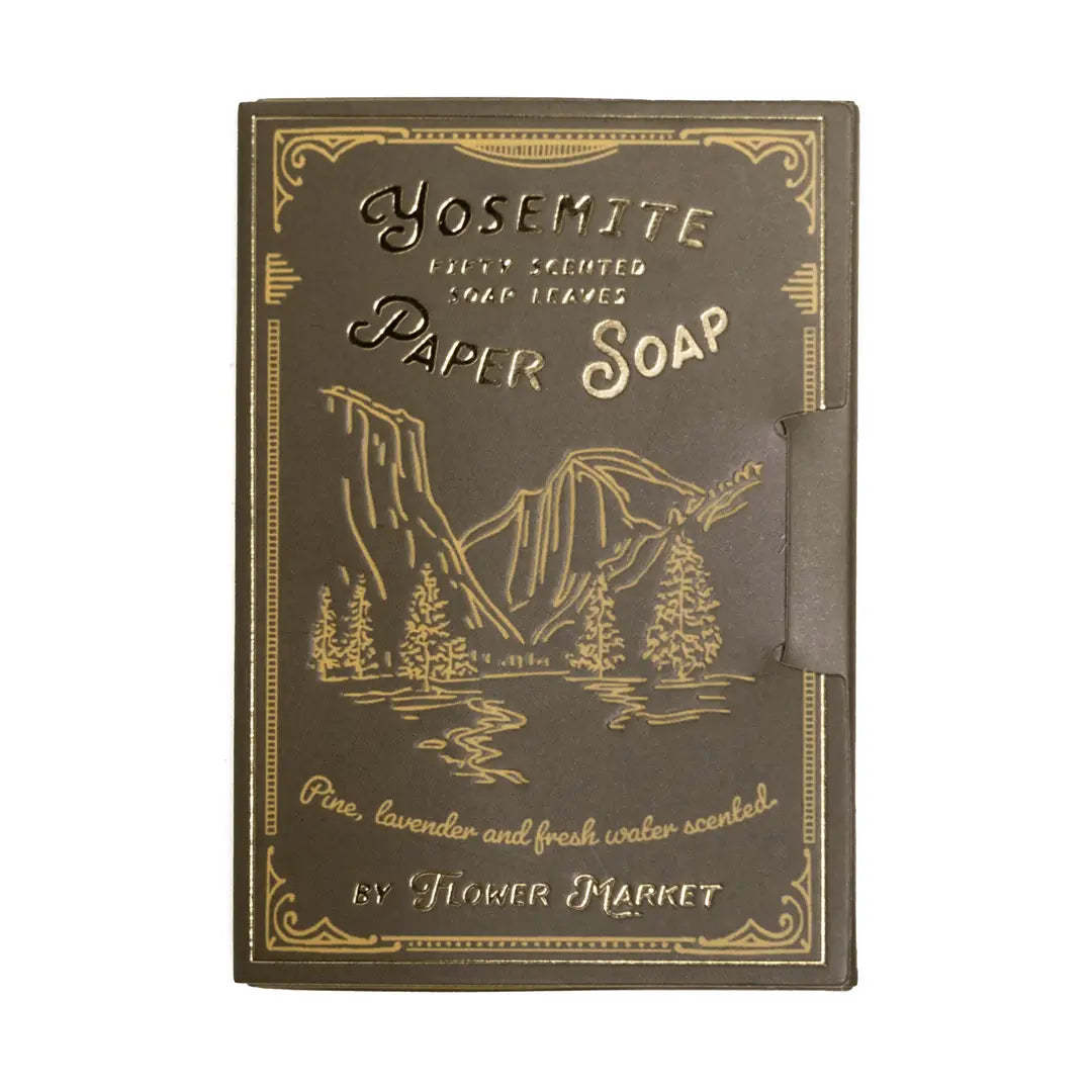 A dark olive book style package of Yosemite paper soap leaves by Flower Market, featuring gold foil mountain and pine tree illustrations, scented with pine, lavender, and fresh water, containing 50 soap leaves.