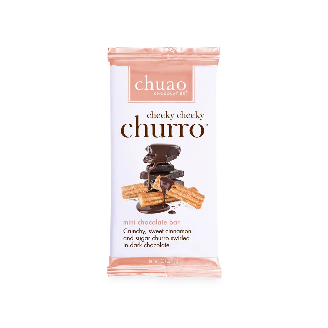 A .39 oz Chuao Chocolatier Cheeky Cheeky Churro chocolate bar featuring a packaging design with stacked dark chocolate pieces drizzled in chocolate and paired with churros dusted in cinnamon and sugar. The label highlights "crafted with joy" and fair trade certified ingredients.