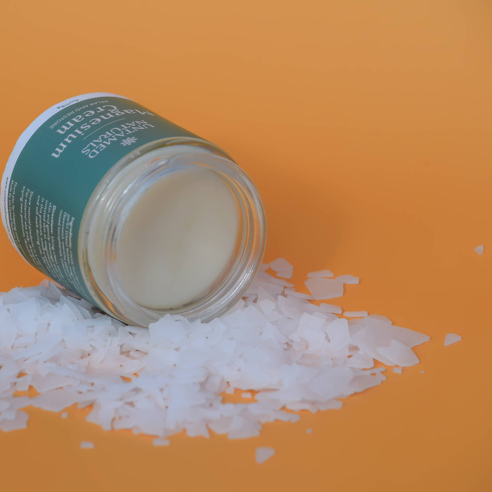 an open jar of magnesium cream on its side with a pile of white flakes and an orange background. Brand: UnTamed Naturals