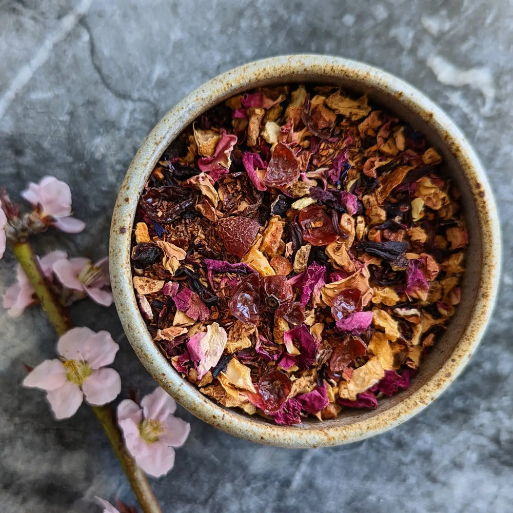 close up view of cherry blossom loose leaf tea in a ceramic bowl and a stem of pink flowers on the side.