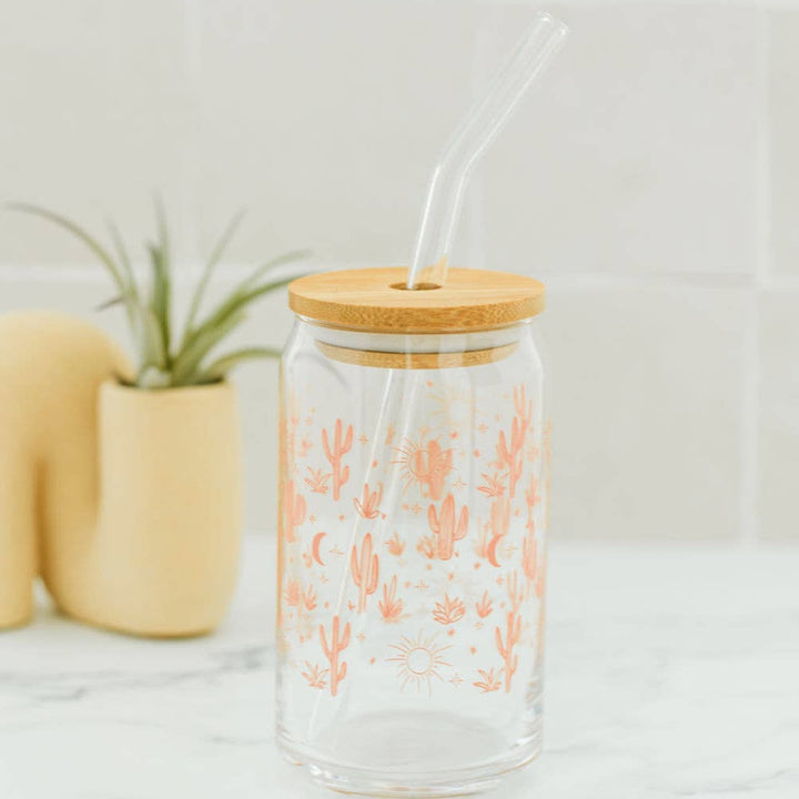 clear glass tumbler with a lid and glass straw featuring an orange cacti and design on a counter with a yellow planter in the background