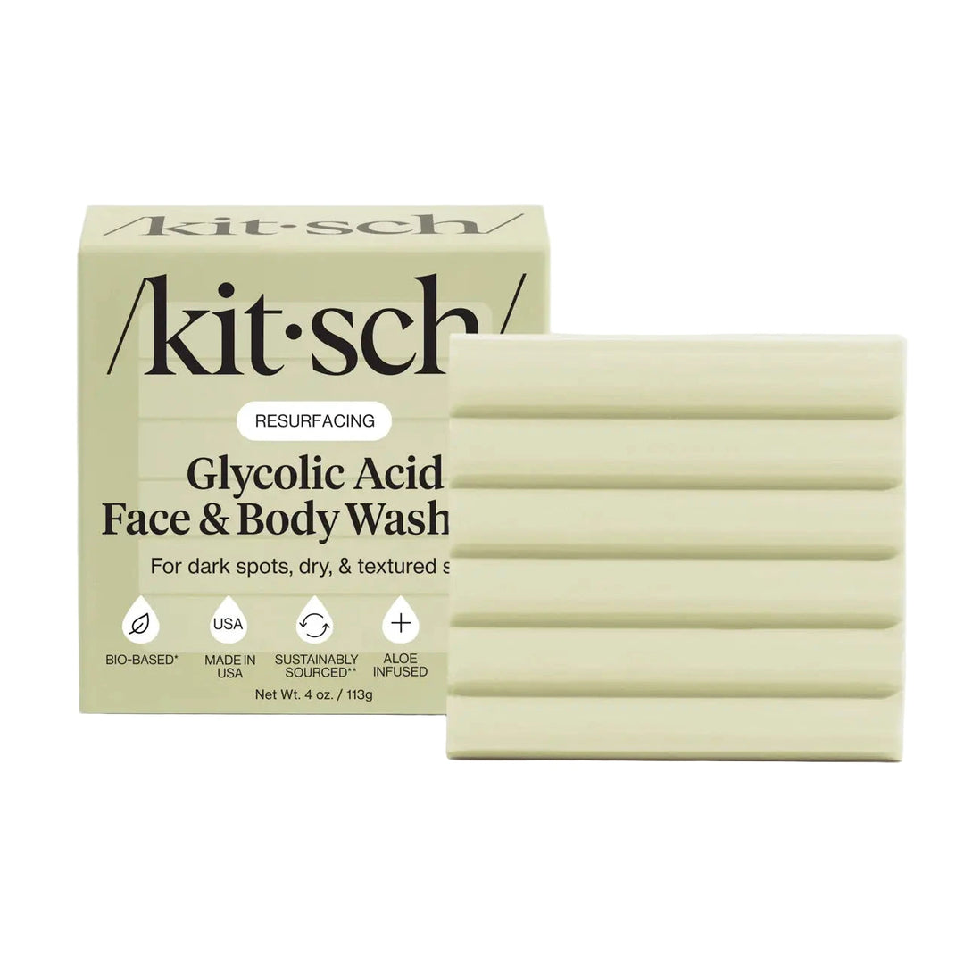 Pale sage /kitsch/ box labeled “Glycolic Acid Face & Body Wash – Resurfacing” shown beside a matching light-green bar with horizontal grooves; icons note bio-based, made in USA, sustainably sourced, and aloe infused; 4 oz.