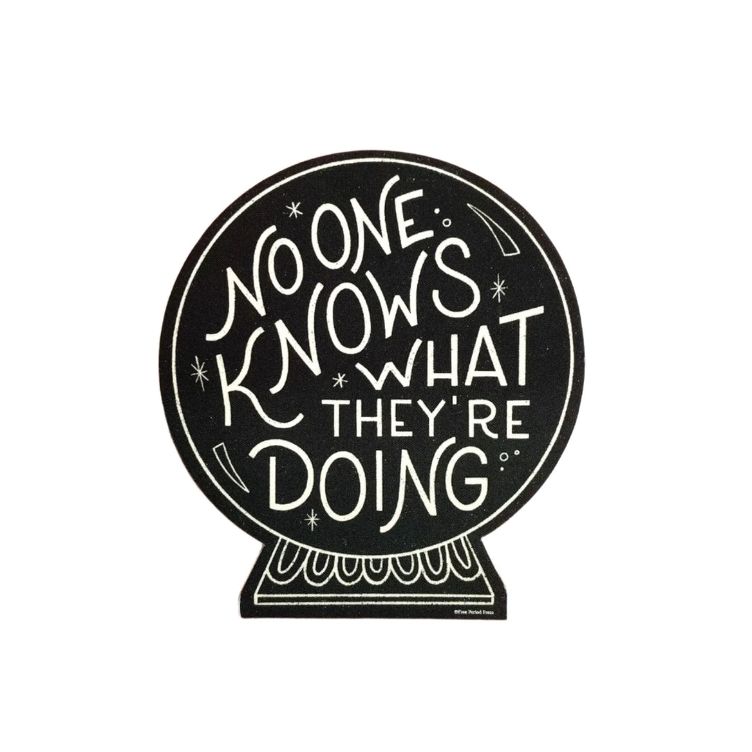 A black sticker shaped like a crystal ball with the phrase "No One Knows What They're Doing" written in a whimsical, hand-lettered style.