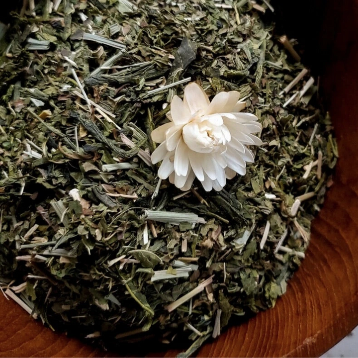 close up view of loose leaf green tea and peppermint in a wooden bowl with a white flower in the center