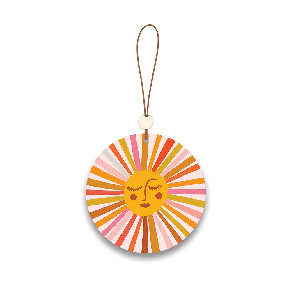 Round car air freshener with a retro yellow sun face and colorful radiating stripes in pink, orange, and red tones, hanging from a brown string with a small cream bead.