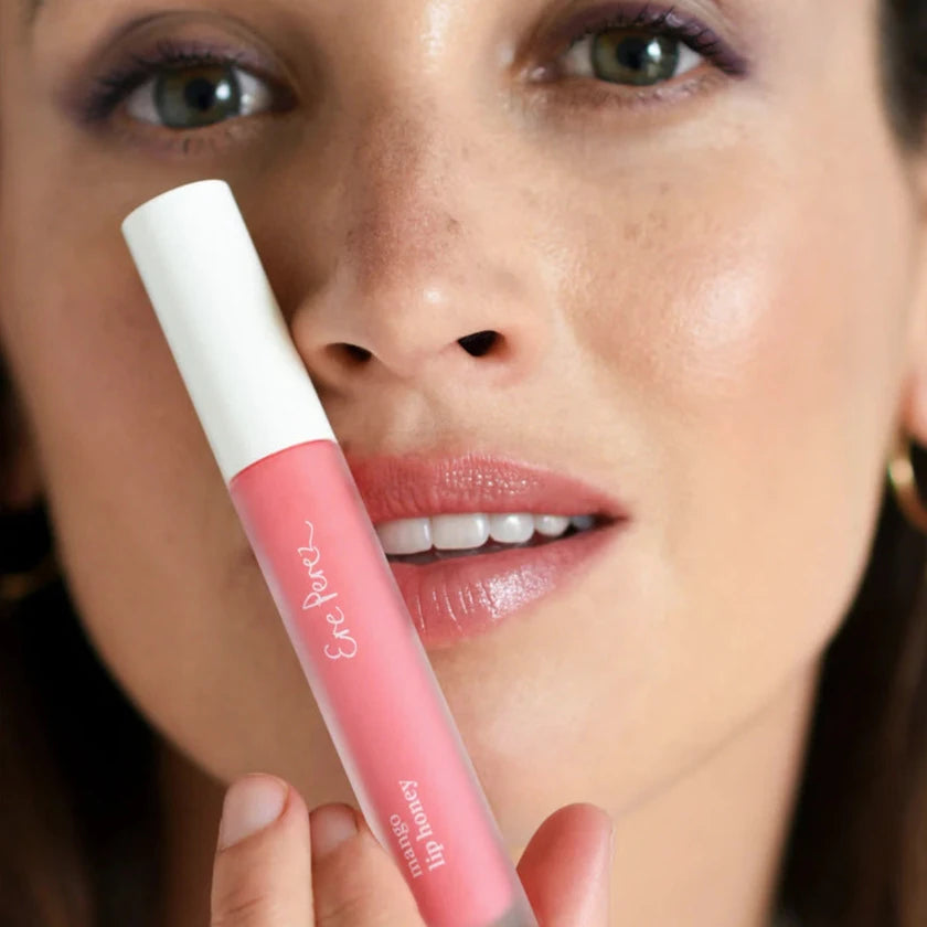 close up of woman holding a tube of lip honey to her face and wearing pink lip gloss.