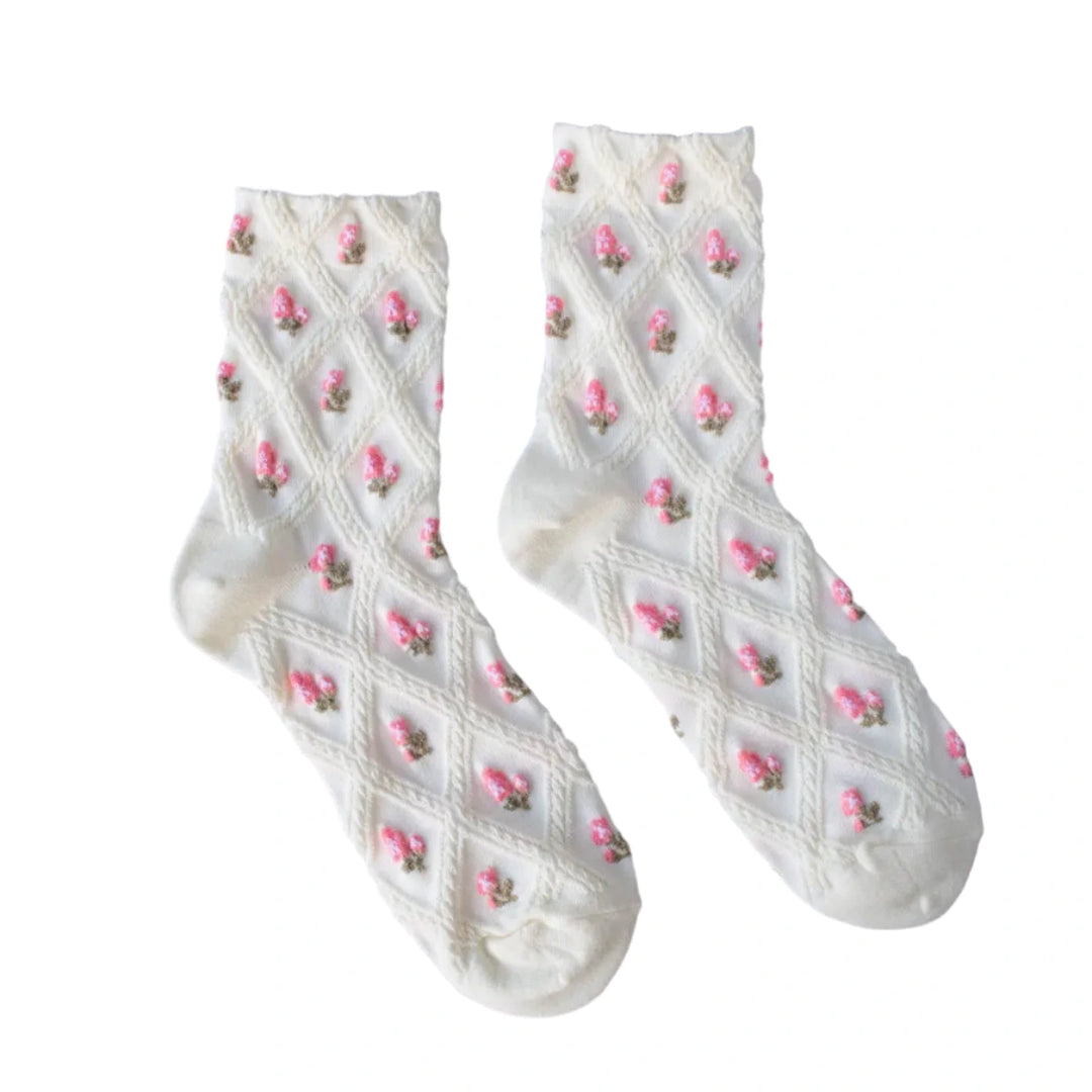 A pair of cream-colored socks with a textured diamond knit pattern and small pink embroidered flowers, laid flat on a gray background