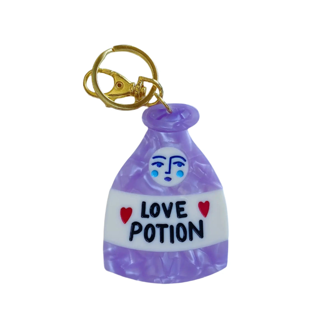 A whimsical keychain shaped like a love potion bottle with the words "LOVE POTION" written in bold, surrounded by red heart accents, attached to a gold clasp. 