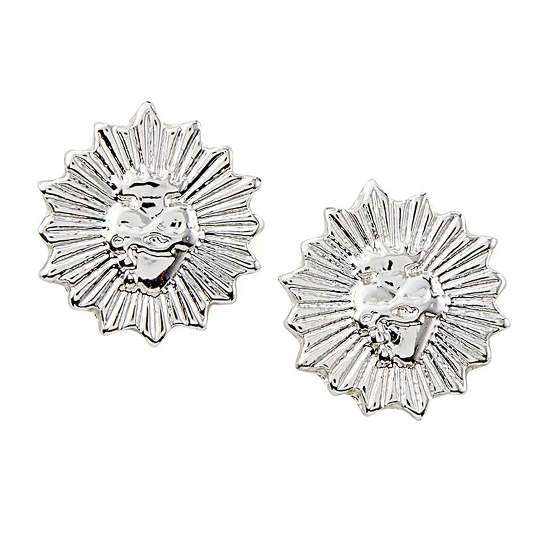 Pair of silver-tone round stud earrings with a sunburst border and a raised flaming sacred heart at the center, shown on a white background.