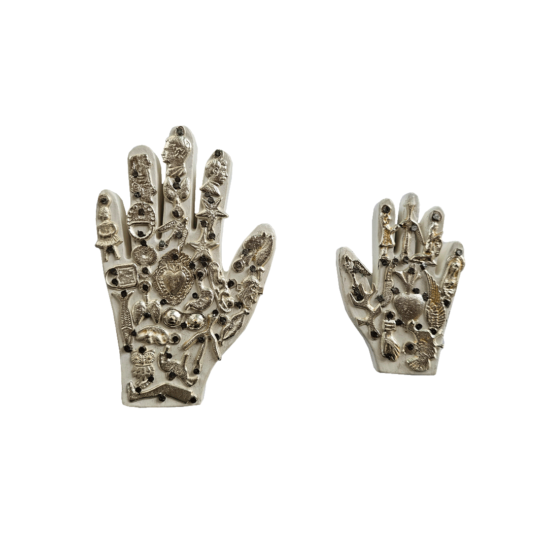 a set of white milagro hands, one larger than the other,  with various styles of milagro charms