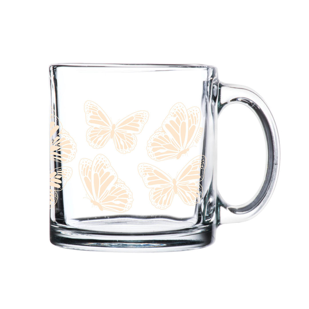 Clear glass mug features a wrap around design of ivory colored monarch butterflies