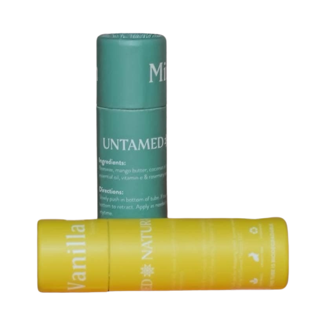 two tubes of lip balm. One is standing straight in green branded labeling and the other is laying on its side with yellow labeling. Brand: UnTamed Naturals