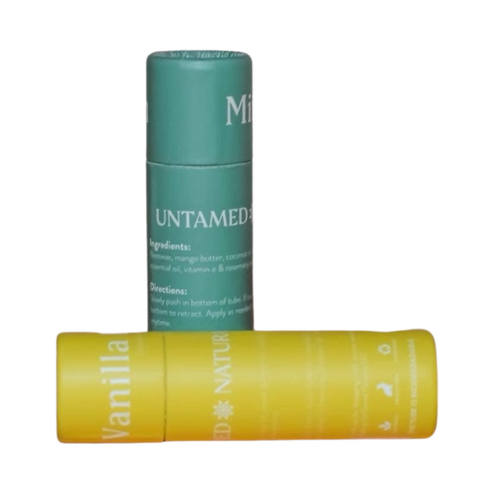 two tubes of lip balm. One is standing straight in green branded labeling and the other is laying on its side with yellow labeling. Brand: UnTamed Naturals