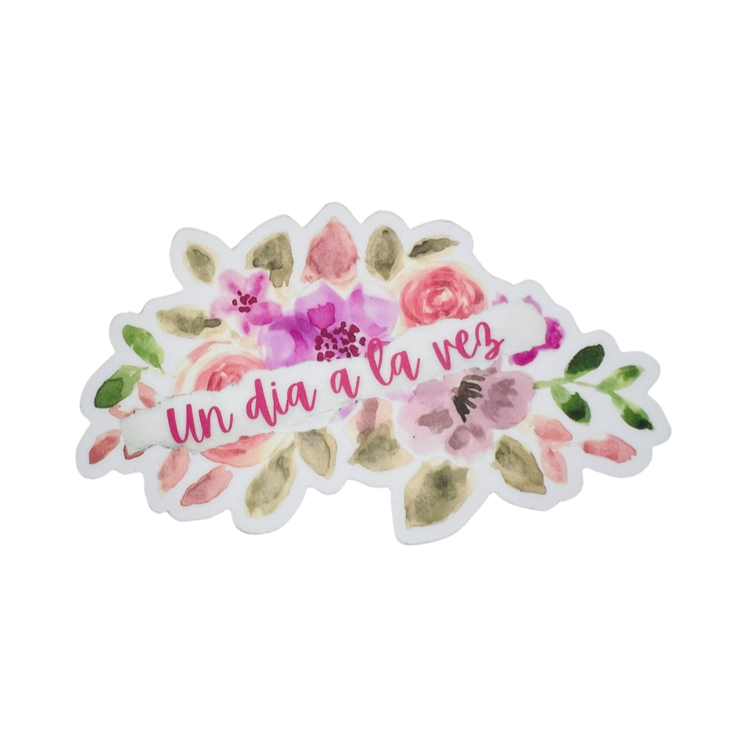 white sticker with flowers of various shades of pink and the phrase Un Dia A La Vez in pink lettering