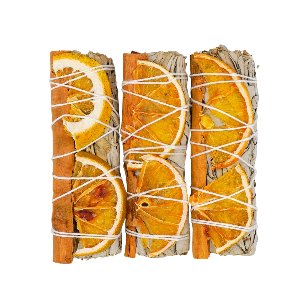 three sage bundles with orange slices and a cinnamon stick tied with white twine
