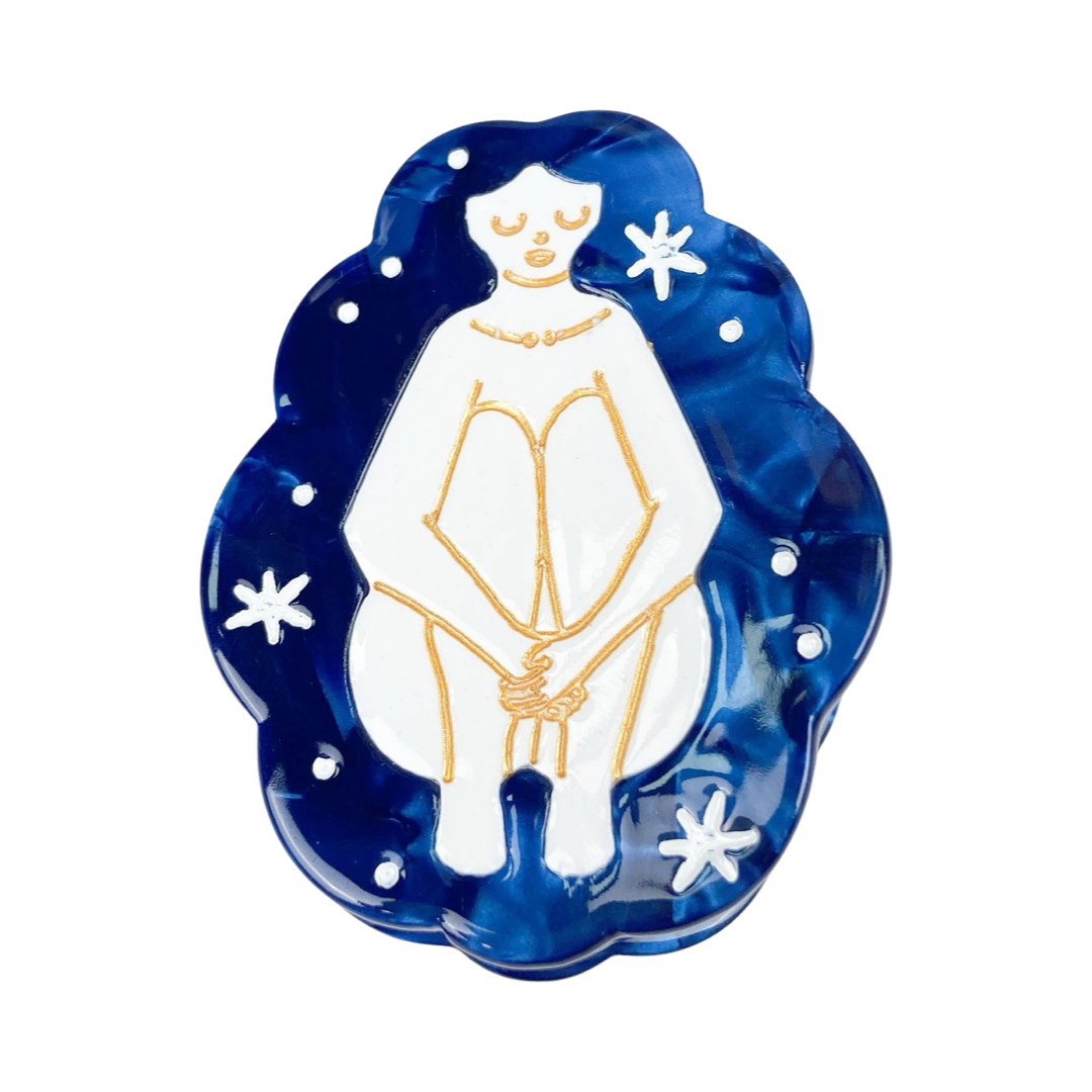 blue hair clip that features an outline of a woman in gold sitting down holding her knees in