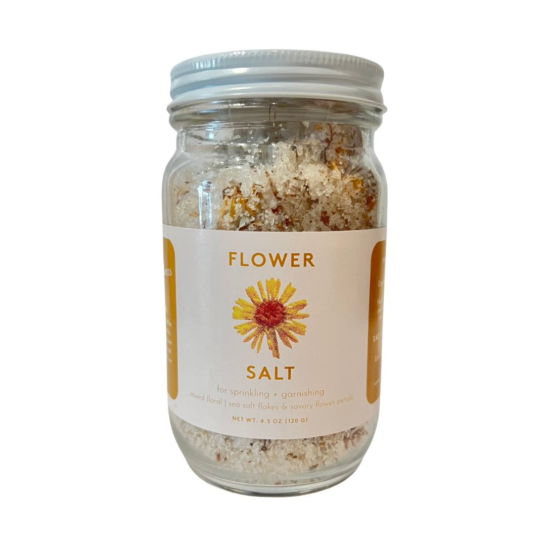 4.5 oz clear jar with salt and dried flower petals with a white brand label and an image of a yellow flower.