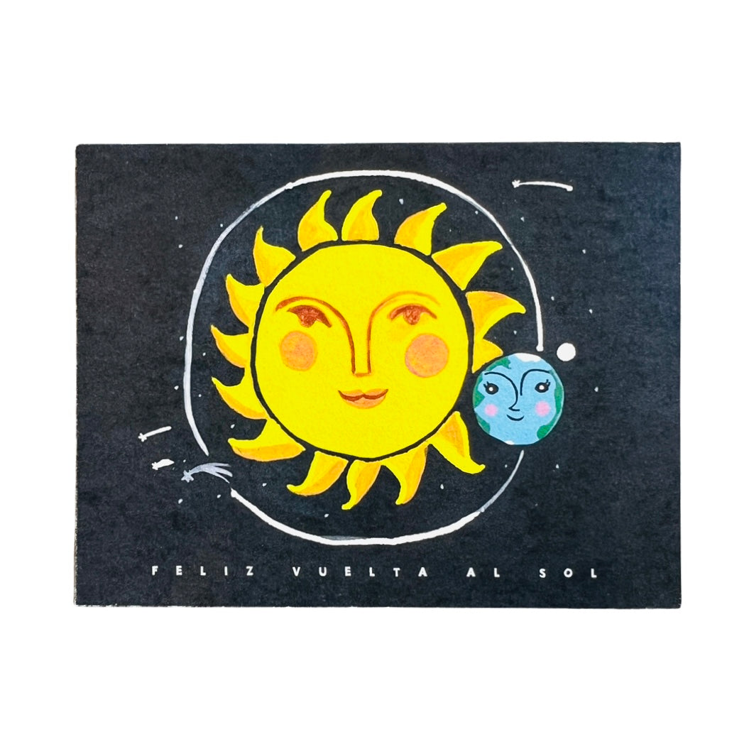 black card with a sun and an orbiting Earth with the phrase Feliz Vuelta Al Sol in whte lettering