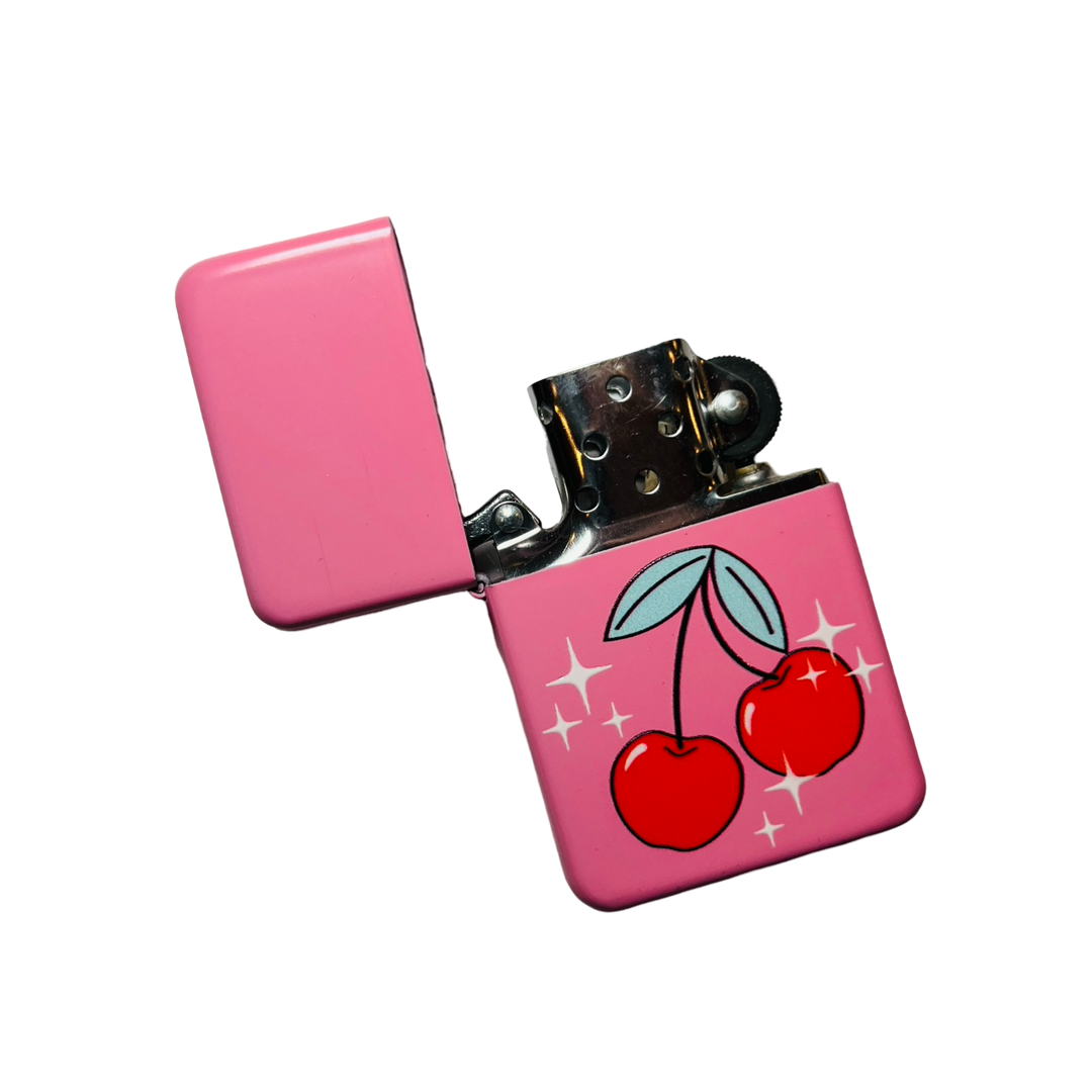 A pink flip-top lighter with a vibrant cherry illustration and sparkling details, featuring a classic metal ignition mechanism.