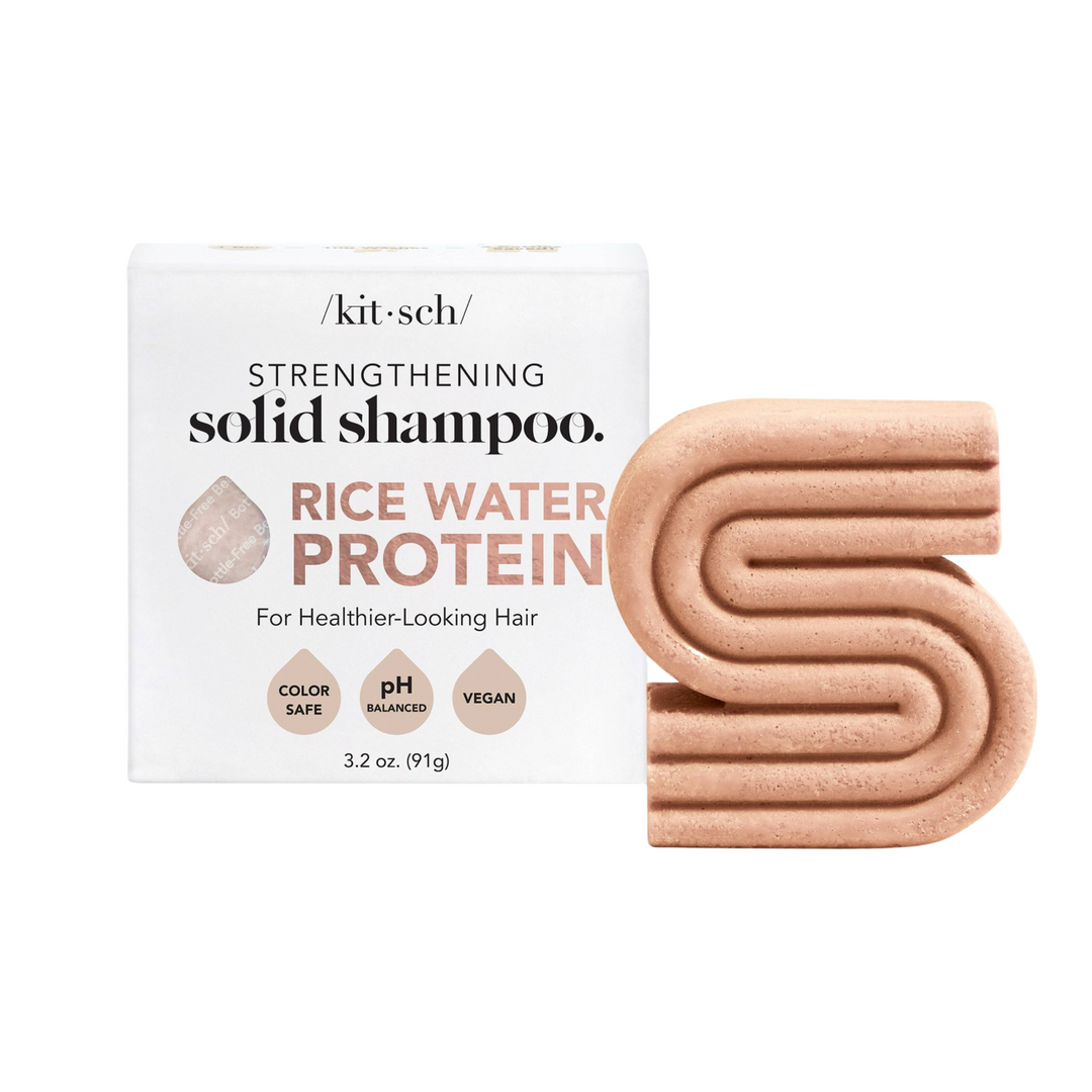 White branded box of shampoo bar and at its side a light terracotta colored bar of shampoo in the shape of the letter "S.". Brand: Kitsch
